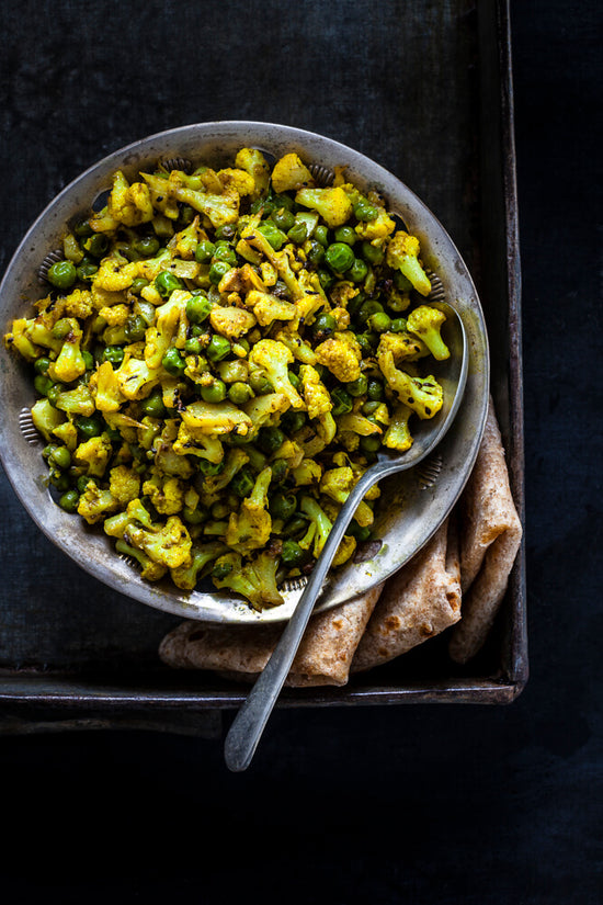 Gujarati style Cauliflower and peas nu shaak in a bowl with spoon inside a tray with folded rotli