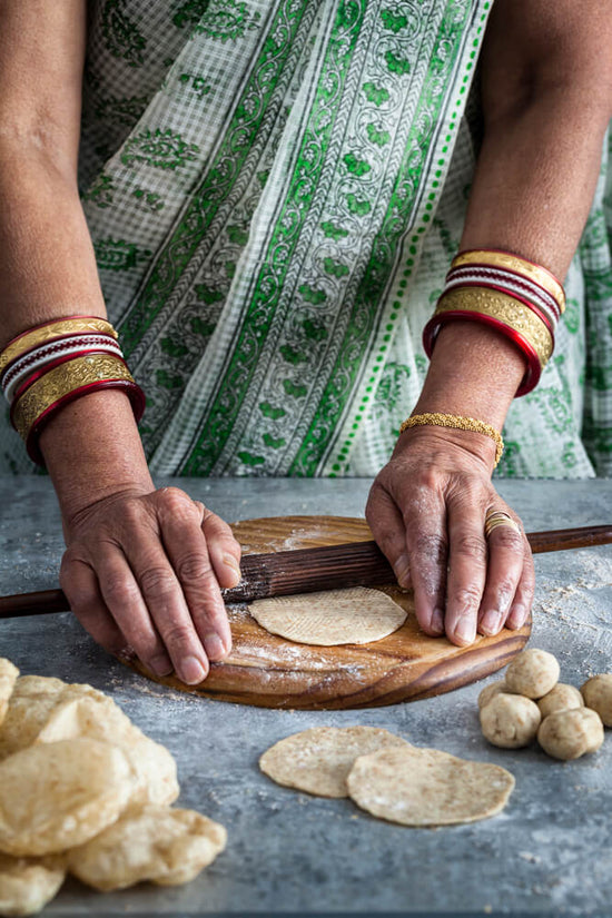 Indian lady in green sari rolling Gujarati puri recipe / poori  with bangles on