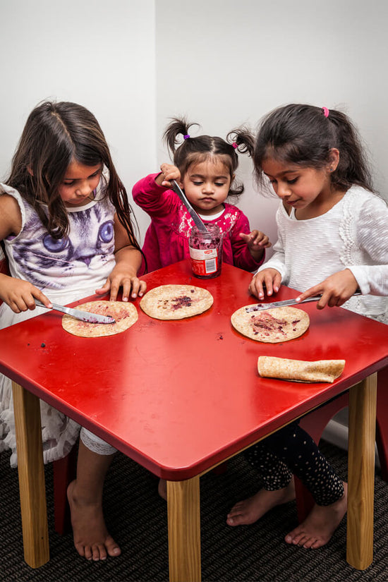 children gathered around red table making jam and rotli