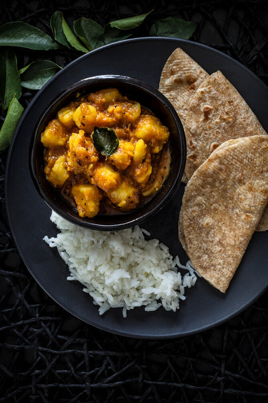 Gujarati Potato curry in a bowl on a plate with rice and rotli