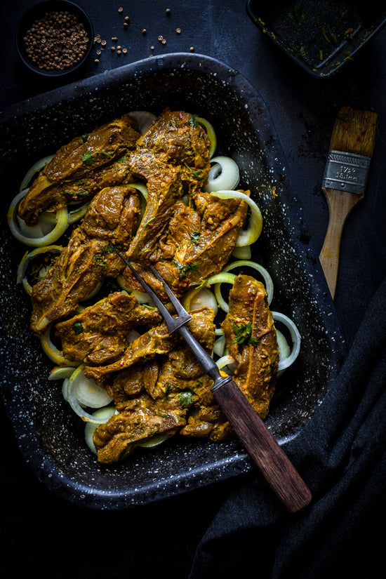 Masala marinated lamb chop on a bed on onion ring inside a baking tray ready to bake