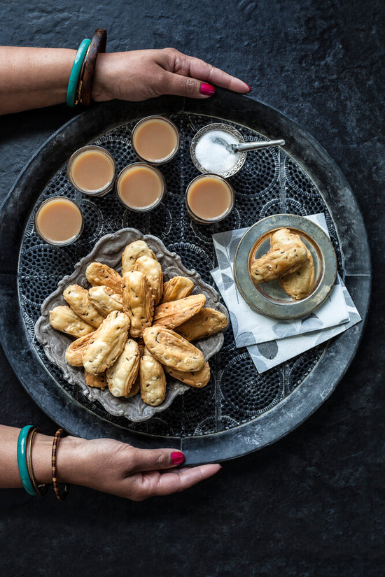 lady in bangles serving banana puri with chai and sugar on a serving tray