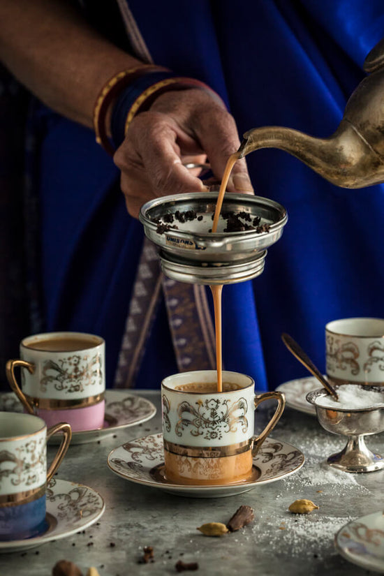 Indian lady in sari, saree pour chai through chai sieve into beautiful decorative teacups