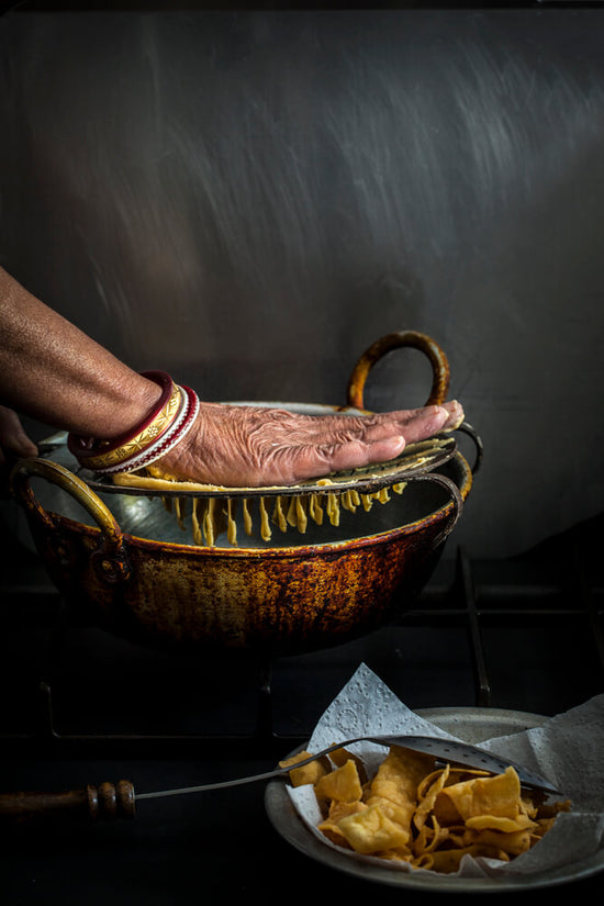 Old Indian Lady hands with bangles making fafda with fafda jarda over kadhi of hot oil