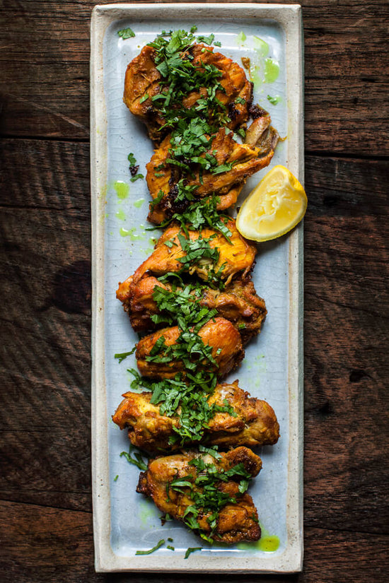Masala Fried chicken on a tray topped with chopped coriander and a slice of lemon