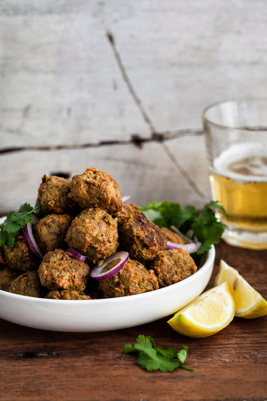 Gujarati Masala lamb meatballs in bowl with lemon slices and glass of beer