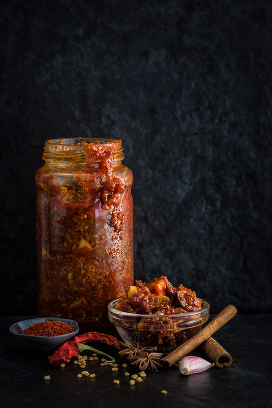 Lemon pickle jar with pickle selection in bowl and pickle spices, fenugreek, chilli, garlic, cinnamon