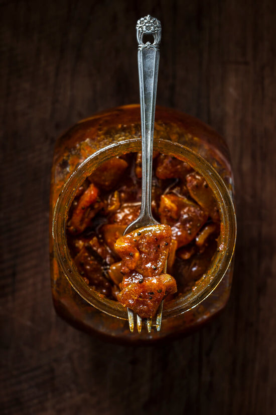 mango pickle on fork with a large jar filled on mango pickles