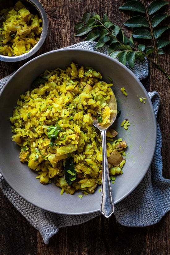 Poha, Gujarati style potato and rice flake dish in a bowl with spoon ready to eat