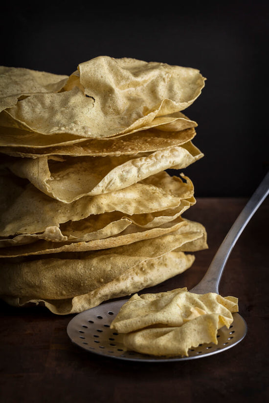 Pappadoms - cooked and layered in a tall pile, one pappadom on a sieve
