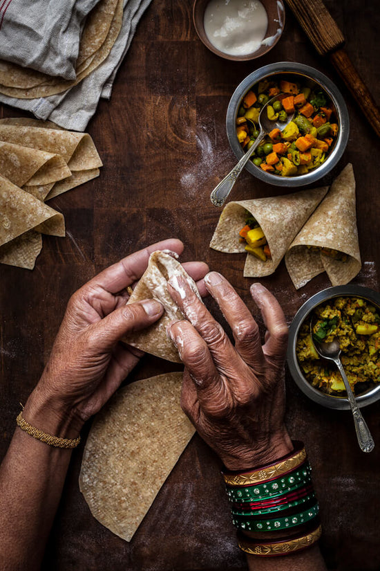 Samosa Making in action with old Indian lady hands with bangles creating samosa cases and bowls of vegetable and meat samosa filling.