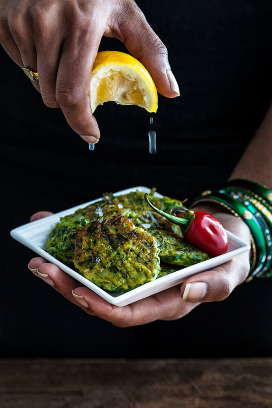 Spinach Fritters on a plater with lemon being squeezed on top and lemon dripping